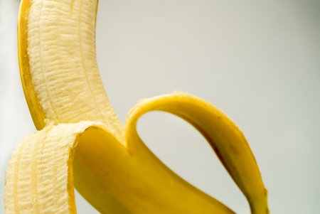 Peeled banana half revealing vibrant yellow pulp on white background ,fresh, ripe, natural snack perfect for healthy eating and dessertsの写真素材