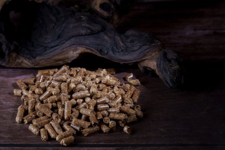 Wood pellets piled on a dark wooden surface with natural wood in the background, showing eco-friendly heatingの写真素材