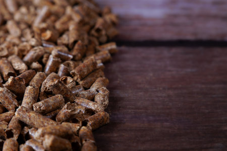 Wood pellets appearing as a renewable energy source for heating, showing biomass fuel on a dark wood...
