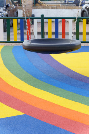 Playground swing hanging over a colorful rainbow-striped rubber safety floor, creating a cheerful atmosphereの写真素材