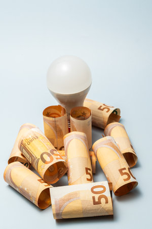 Light bulb surrounded by rolled up 50 banknotes, symbolizing rising energy prices and financial strainの写真素材