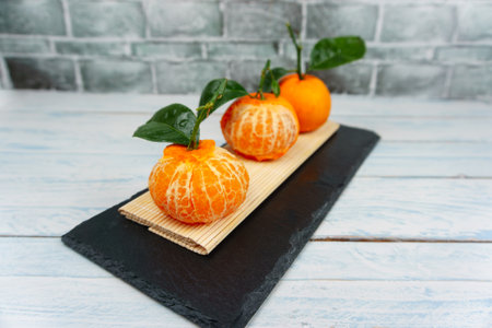 Freshly peeled tangerine and whole citrus fruit artfully arranged on a slate plate, highlighting healthy eatingの写真素材