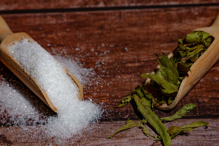 Stevia leaves and white granulated sugar in wooden scoops on a rustic wooden background, illustrating healthy sweet choiceの写真素材