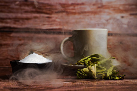 Sugar bowl, dried tea leaves, and a steaming cup creating a cozy atmosphere on a rustic wooden tableの写真素材