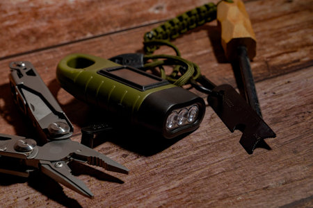 Survival gear kit, including a multitool, a solar flashlight, and a fire starter, arranged on a rustic wooden surfaceの写真素材