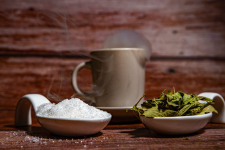 Hot tea with rising steam, offering natural stevia leaves and white sugar as sweetener options on a rustic wood backgroundの写真素材