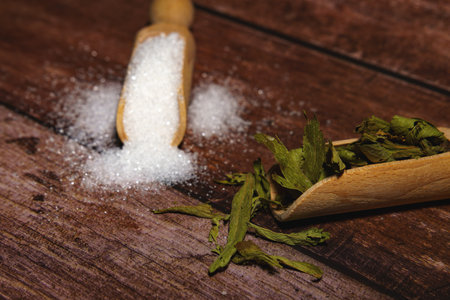 Stevia leaves and granulated sugar in wooden scoops showing natural sweetener alternative. Healthy dietary choice conceptの写真素材