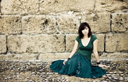 Sad young woman sited in antique stone backgroundの写真素材