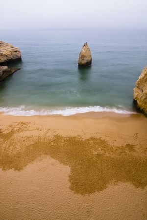 Empty beach with a rock in the middle of the bay.の写真素材