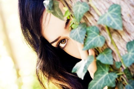 Young beautiful woman observing behind leaves.の写真素材