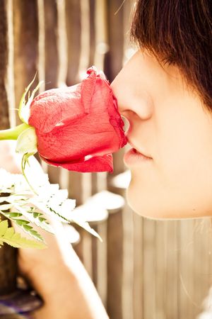 Young anonymous woman smelling a red rose behind metal fence.の写真素材