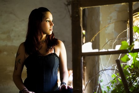 Young beautiful goth girl looking at broken window.の写真素材