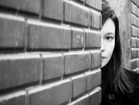 Woman looking behind a brick wall.の写真素材