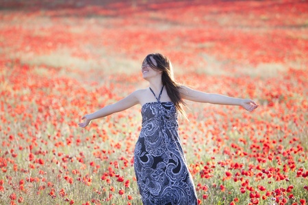 Young beautiful woman with raised arms on a poppies field.の写真素材