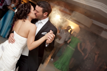 Kissing just married couple dancing in front of their unrecognizable friends.の写真素材