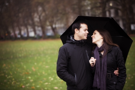 Young sweet couple sharing umbrella and smiling each otherの写真素材