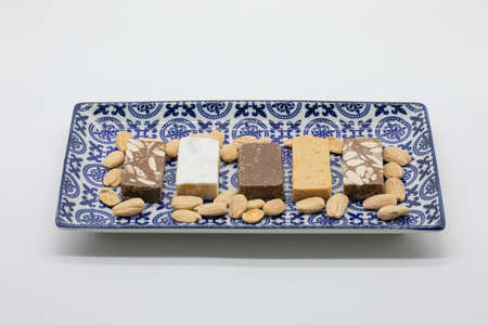 Assortment of kinds of nougat and almonds in decorated ceramic tray, isolated on a white background