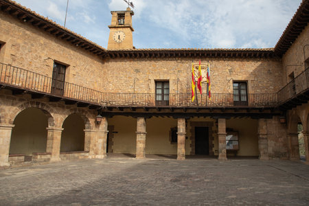 Historic stone building with arches, flags, and clock under blue skyの写真素材