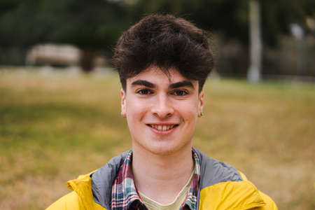 Caucasian happy guy standing in university campus. Portrait of teenage male student looking at camera in a collegeの写真素材