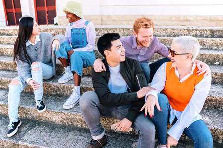 Group of friends enjoying the weekend sitting outdoors. Multiethnic people talking in stairs.の写真素材