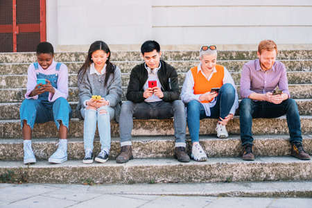 beautiful young people in casual clothes using mobile phone while sitting together on the stairs.の写真素材