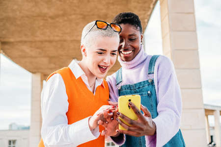 Two beautiful young girls having fun using app on a smart phone. A pair of friends searching offerts on internet.の写真素材