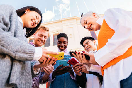 Five cherful friends using his cellphone and having fun together. Low angle of multiethnic group of happy people sharing media.の写真素材