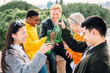 Multiethnic friends drinking bottles of beers and having fun together outdoors.の写真素材