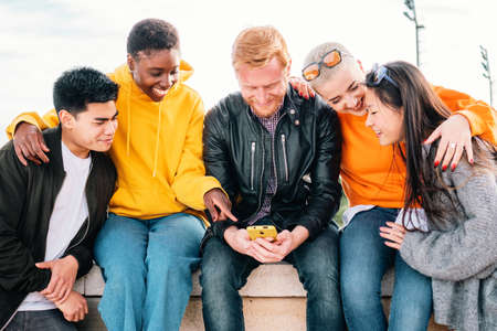 Five young friends watching a video in a mobile phone and smiling together.の写真素材