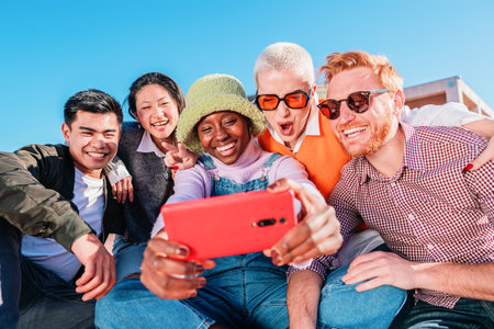 Five young multiethnic friends taking a selfie together outdoors under blue sky.の写真素材
