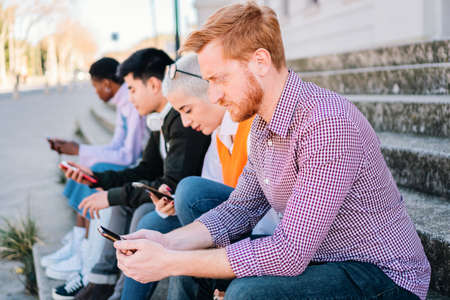 Friends using smartphones and browsing on internet sitting outdoors.の写真素材