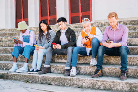 group of friends browsing with their mobile phones sitting outdoors.の写真素材