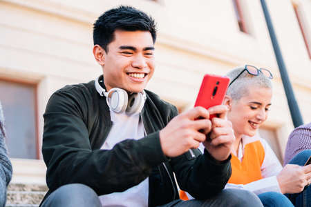 Young man touching a mobile screen sitting outdoor and smiling.の写真素材