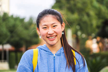 Young chinese lady student smiling looking at camera at the high school. Close up portrait of cute asian girl standing and laughing at campus.の写真素材
