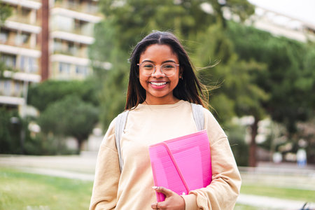 Happy hispanic school girl with glasses smiling and laughing out of class. Cute teenage student standing at the university campusの写真素材