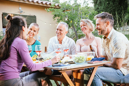 Group of mature adult friends toasting his wine glasses and beers and having fun in a dinner party at the back yard. Lifestyle concept.の写真素材