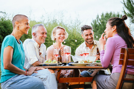 Group of adult friends or familly talking and having fun sitting at table in a dinner party in a back yard. Lifestyle concept.の写真素材