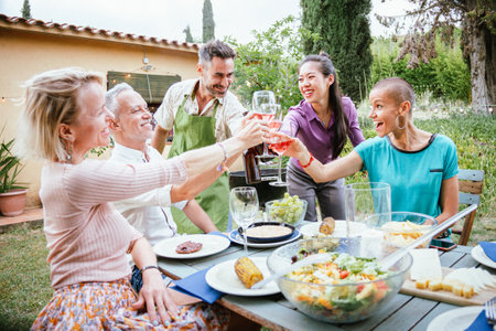 Happy adult friends smiling and toasting wine glasses at celebration at house backyard. Two mature men and three women having fun toguether at weekend party. Lifestyle concept.の写真素材