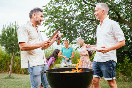 Two adult friends or family men talking and smiling, cooking and grilling in a barbeque party with...