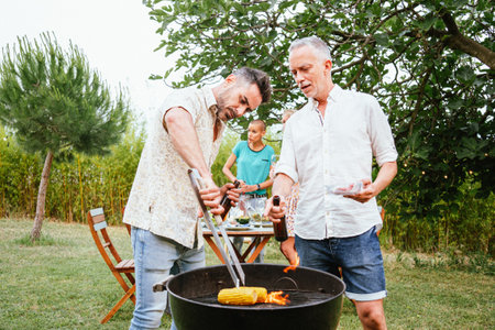 Two men cooking and toasting beers on a barbeque in countryside. At background, three women friends...