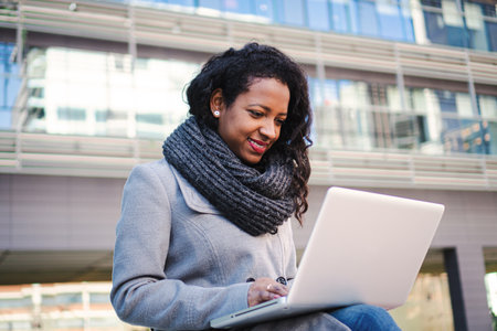 Portrait of business woman looking laptop computer outside office. Smiling young girl near notebook outdoor at remote workplace. Business conceptの写真素材