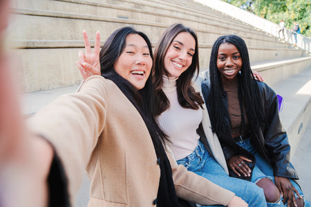 Happy group of multiracial young women taking a selfie portrait smiling at camera. Three diverse girls having fun outdoors. Best friends taking a photo.の写真素材