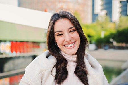 Caucasian young woman smiling and looking at camera with perfect white teeth. Close up portrait of beautiful happy female with white clothes standing outdoors.の写真素材