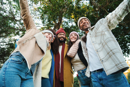 A group of multiracial young friends having fun together in a park doing autumn weekend activities wearing coats and hats. Five happy people smiling and walking outdoors. Lifestyle concept.の写真素材