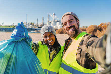 A environmental activist or volunteer multiracial couple picking up trash og the beatch, and taking a selfie portrait smiling looking at camera showing a recycle plastic bag.の写真素材