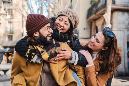 Multiracial group of three happy friends having fun and laughing together. Bearded male giving his girlfriend a piggyback ride. Tourist hugging each other and enjoying a travel trip in Europe.の写真素材