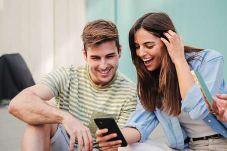 Two teenage happy friends watching funny videos browsing on internet app with a smartphone and smiling together. Caucasian couple using a cell phone to post in a social media and chatting onlineの写真素材