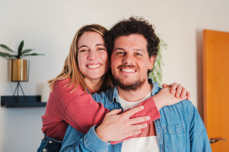 Close up portrait of heterosexual young caucasian couple embracing together at home living room, looking at camera with love attitude. Front view of married people hugging and smiling, relationshipの写真素材