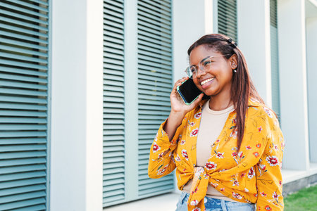 African american young female student talking on a smartphone. One hispanic woman having a mobile phone call standing outdoors, laughing and smiling in a friendly conversation withの写真素材