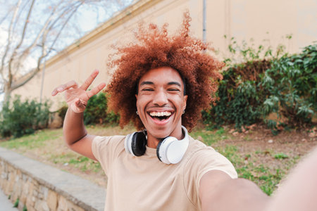 happy african american guy with afro hair taking a selfie portrait. One teenager having fun and laughing outdoors. Joyful man with toothy smile having a video call. Successfulの写真素材